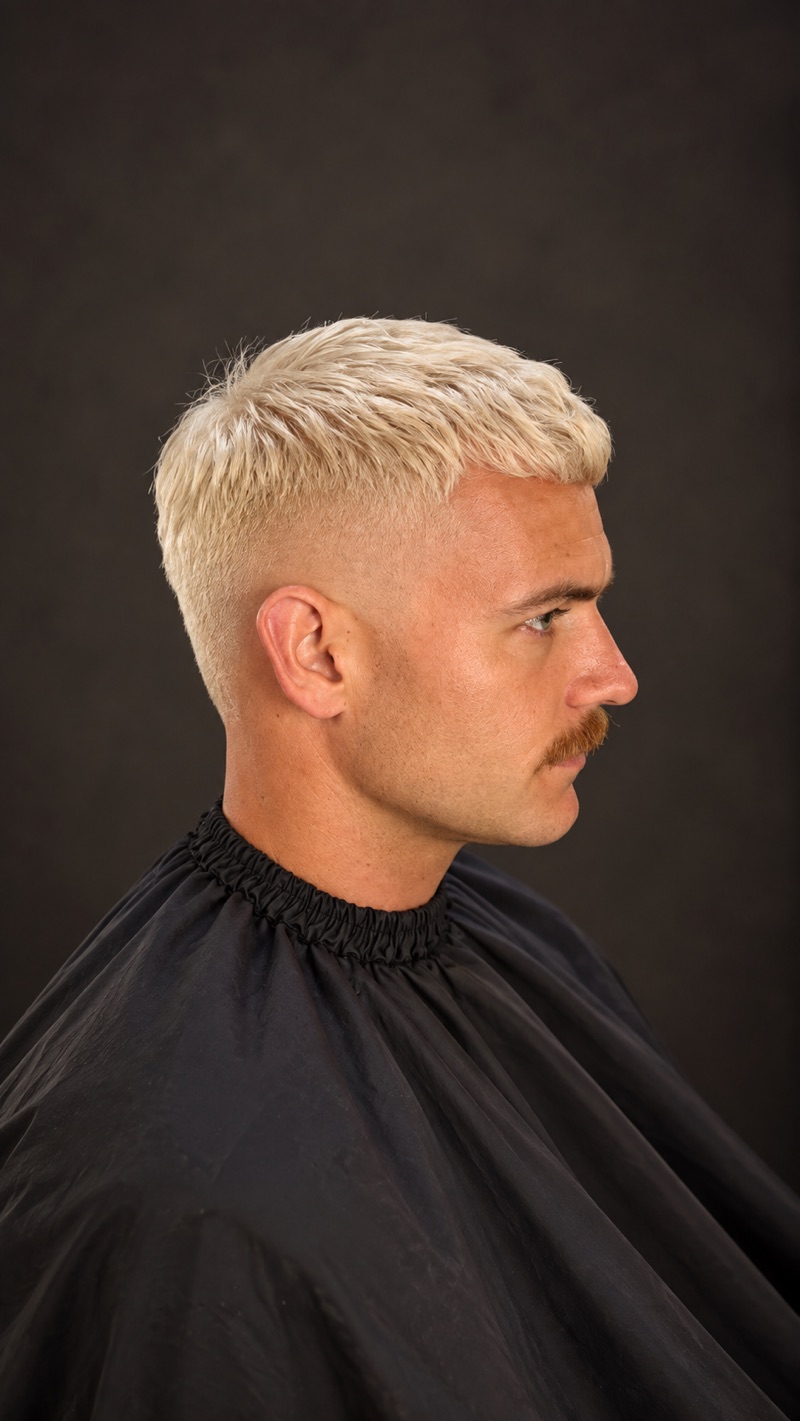 Corte corto con cabello platinado y bigote, vista de perfil